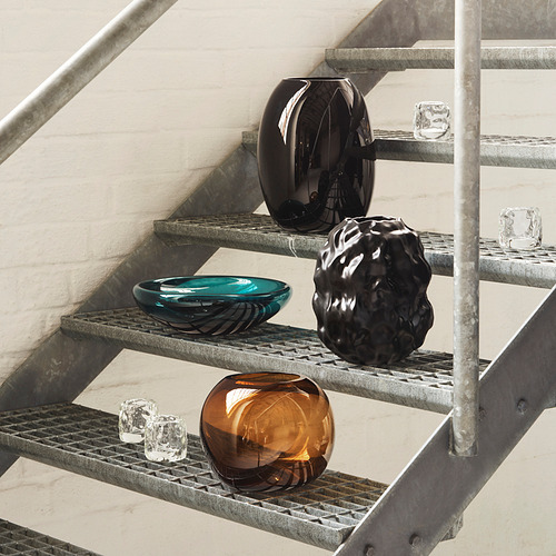 Decoración de vidrio en escalones de metal: piezas negras, marrones, verde azulado y transparentes, con piezas más grandes en negro y marrón.