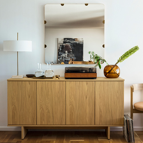 Sala de estar moderna con espejo sobre el gabinete, obras de arte reflectantes. Incluye lámpara, jarrones y tocadiscos.