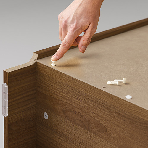 Persona colocando pequeñas clavijas blancas sobre muebles de madera marrón.