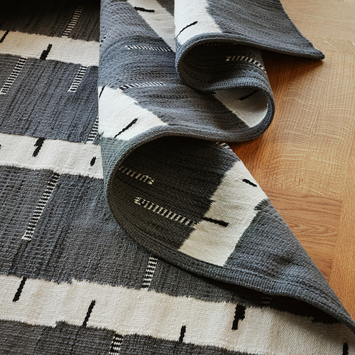 Alfombra de lana tejida a mano con diseño de abedul gris sobre suelo de madera, que muestra artesanía de alta calidad.