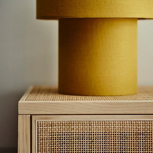 Lámpara amarilla con base de madera sobre mueble de ratán tejido.