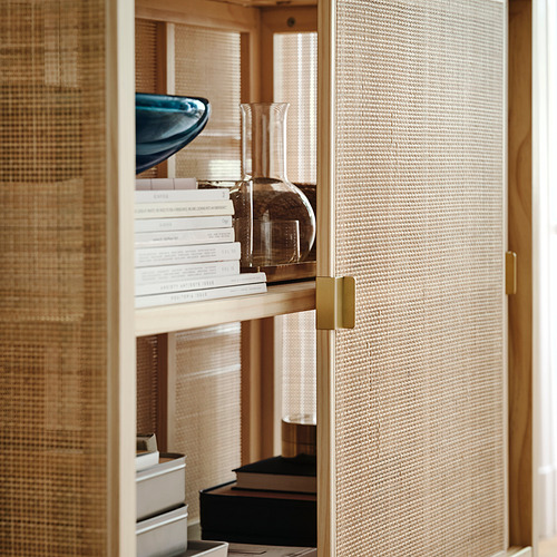 Mueble de ratán con patas ajustables, puertas correderas, manijas de latón, sosteniendo libros y jarrones.