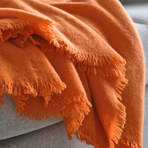 Manta de color naranja brillante doblada cuidadosamente, mostrando un material de lana suave y texturizado con bordes de flecos.