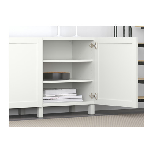 Aparador blanco BESTÅ con estantes ajustables y puertas de cierre suave, se muestra abierto con libros apilados en su interior.