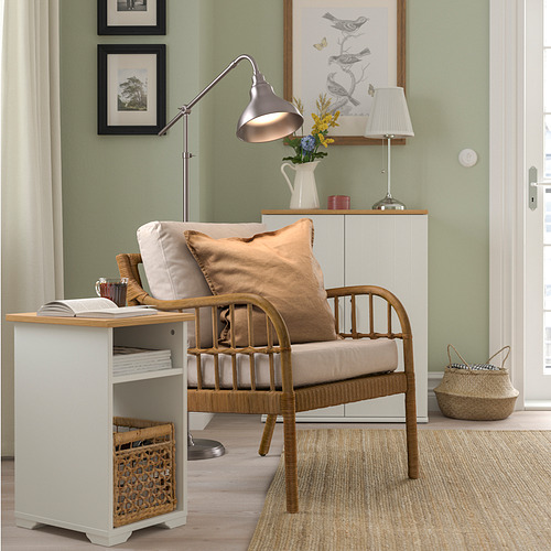 Mesa auxiliar SKRUVBY blanca con revista y cesta, junto a silla de madera sobre alfombra beige.