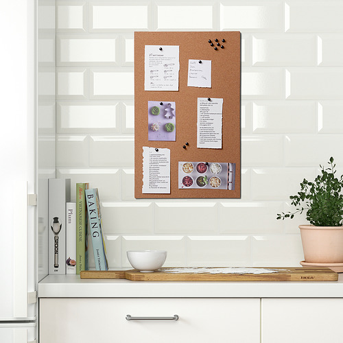 Tablero de notas de cocina con notas, fotos y alfileres en corcho, montado en pared de azulejos.