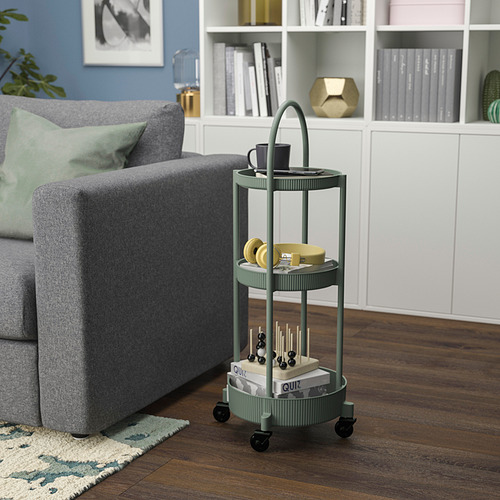 Pequeño carrito rodante verde de 3 niveles junto a un gran sofá gris, con tazas y libros.