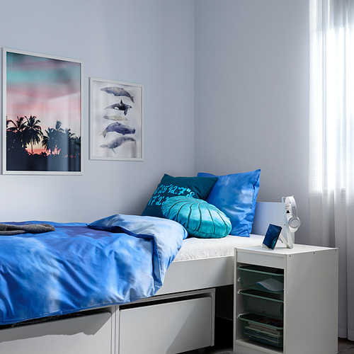 Dormitorio con ropa de cama y almohadas azules, arte de pared a juego, con una unidad de almacenamiento TROFAST blanca al lado.