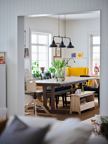 Comedor luminoso con mesa de madera, sillas amarillas, banco negro y lámparas colgantes.