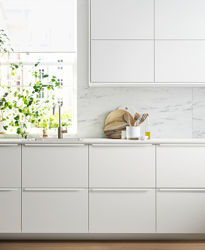 Cocina blanca moderna con placa para salpicaduras de mármol, gabinetes elegantes, fregadero de acero inoxidable, utensilios de madera y planta verde.