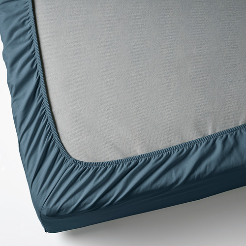 Una sábana azul entallada que cubre una esquina de colchón gris, mostrando bordes elásticos.