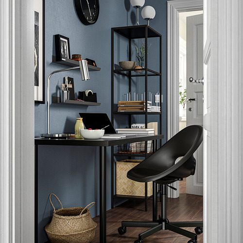Configuración moderna de oficina en casa: escritorio negro, silla elegante, estantería con accesorios y pared azul.