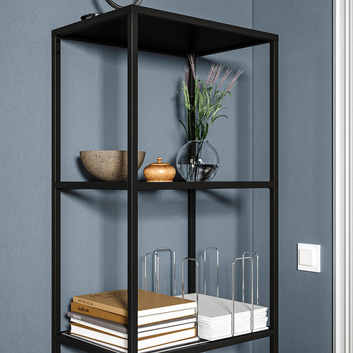 Estantería negra con fondo azul. Parte superior: cuenco, jarra, jarrón con flores. Medio: libros, organizadores. Moderno, minimalista.