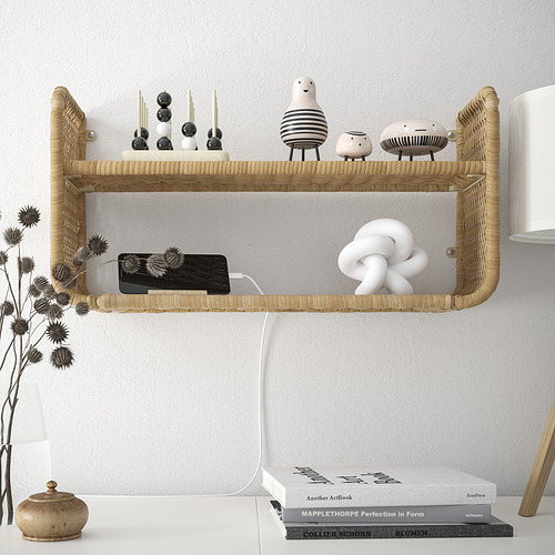 La estantería de pared, FRYKSÅS, contiene artículos decorativos y carga dispositivos. Muestra ratán natural, decoración pequeña y grande, y configuración de carga del teléfono.