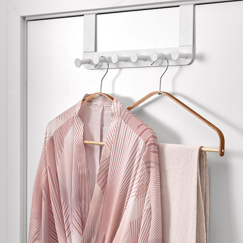 Una bata estampada de color rosa claro cuelga de una percha de bambú, suspendida de un estante de gancho blanco sobre la puerta.