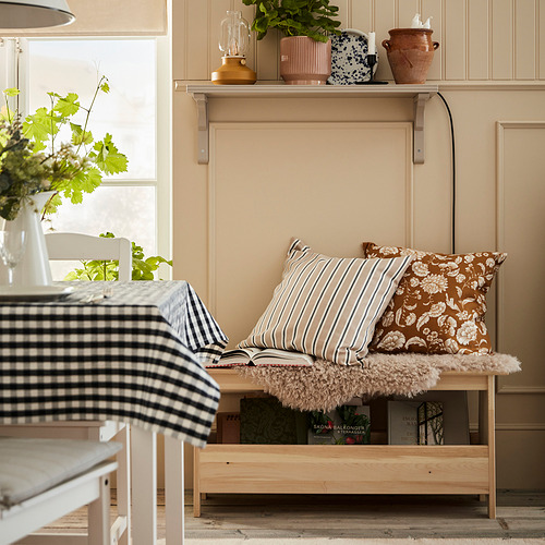 Acogedora habitación con banco de pino, almohadas florales, plantas y tela a cuadros.