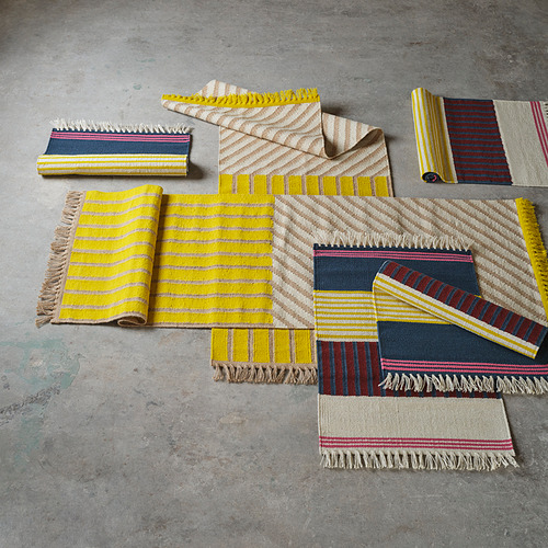 Alfombras MÄVINN tejidas a mano en amarillo, azul, rojo en el suelo. Lana, yute con rayas. Colores vibrantes.