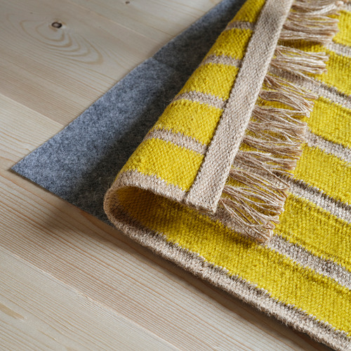 Alfombra de rayas amarillas y beige con flecos sobre suelo de madera.