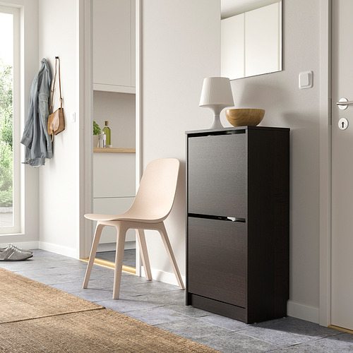 Entrada minimalista con zapatero negro, silla, espejo, lámpara, cuenco, abrigo.