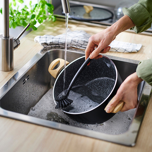 Persona lavando una sartén negra con un cepillo negro en el fregadero de la cocina.