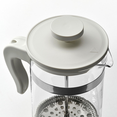 Moderna cafetera de vidrio con mango y tapa blancos, borde plateado y émbolo para la preparación.