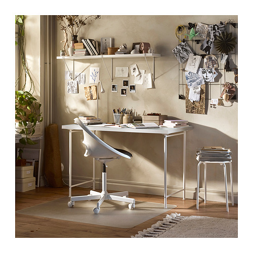 Moderno escritorio blanco con patas ajustables, con una silla ergonómica y varias decoraciones artísticas en una pared de tonos neutros.