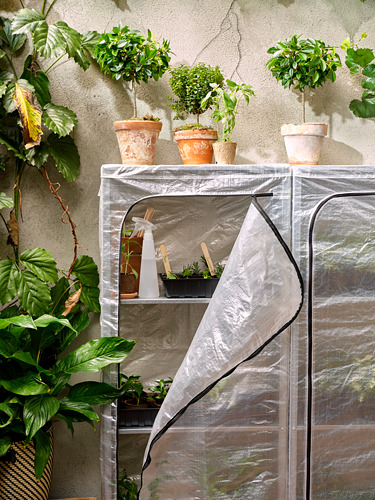 Invernadero interior con estante HYLLIS, cubierta transparente, varias plantas en macetas, herramientas en el interior.