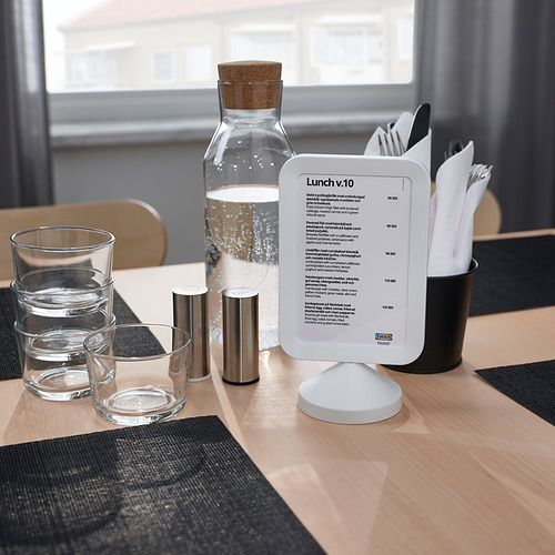 Una mesa de café con un tablero de menú que muestra texto en un marco, vasos, cubiertos, servilletas y una jarra de agua.