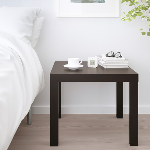 Pequeña mesita auxiliar de ikea LACK junto a la cama con taza, reloj, libros y vasos.