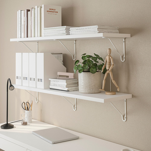 Estantes blancos montados en la pared con libros, carpetas, una planta en maceta y una figura de madera.