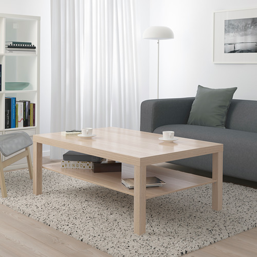 Moderno salón con mesa de centro LACK, sofá gris, alfombra, estantería y lámpara de pie.