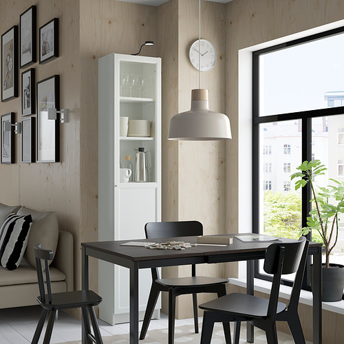 Comedor moderno con librería Billy, mesa negra y sofá gris. Gran ventana, reloj y lámpara colgante.