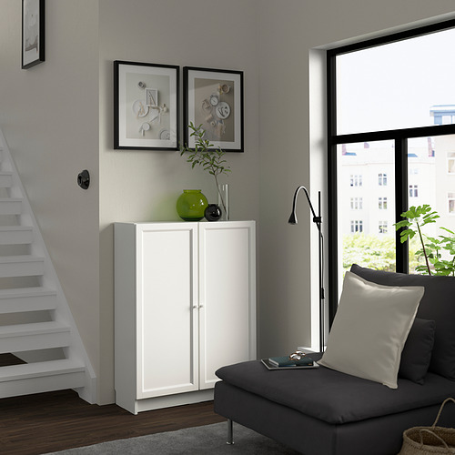 Habitación moderna con librería BILLY blanca, sofá gris, gran ventanal y elementos decorativos.