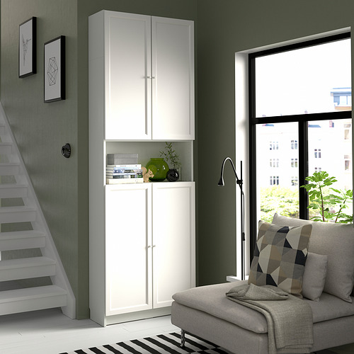 Sala de estar moderna con estantería blanca BILLY, sofá gris, ventana grande y detalles verdes.