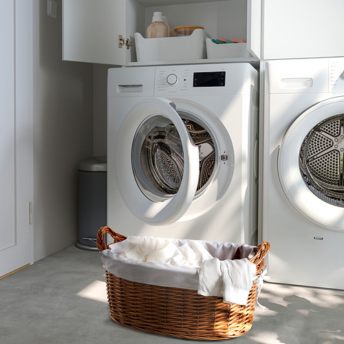 Lavadero moderno con lavadora blanca, secadora y cesta de mimbre llena de ropa blanca.