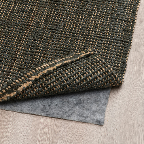 Alfombra de yute verde oscuro sobre suelo de madera, base gris, tejida plana para facilitar el mantenimiento y la calefacción.