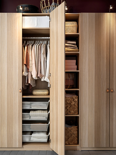 Open light wood wardrobe displaying neatly folded clothes, accessories, and organized storage baskets.