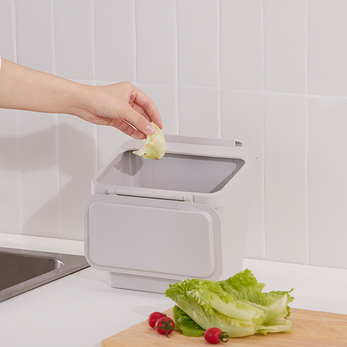 Colocando a mano la cáscara de lechuga en el cubo de basura de cocina SKOLÄST con la tapa abierta, colocado en la encimera cerca del fregadero.