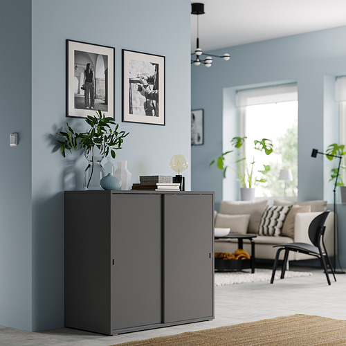 Mueble VIHALS gris en salón moderno con paredes azules y cuadros enmarcados en blanco y negro, con puertas correderas y elementos decorativos en la parte superior.