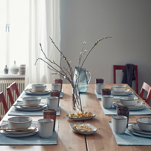 Mesa de comedor rectangular con sillas rojas, platos, tazones, tazas y una jarra azul con bocadillos.