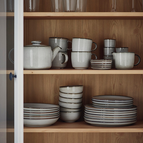 Vajilla GLADELIG colocada sobre estantes de madera; tazas, tazones, platos y teteras de color arena; cuidadosamente apilados; Diseño minimalista.