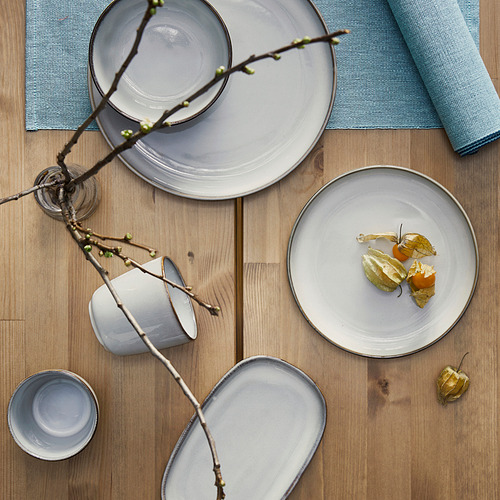 Vajilla GLADELIG ambientada en azul claro sobre mesa de madera con platos y taza.