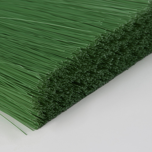 Primer plano de una escoba verde de cerdas rectas, tumbada sobre una superficie blanca.