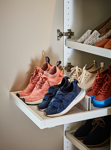 Zapatero con zapatillas de colores, que incluyen pares melocotón, azul, blanco y rojo, cuidadosamente organizados en estantes blancos.