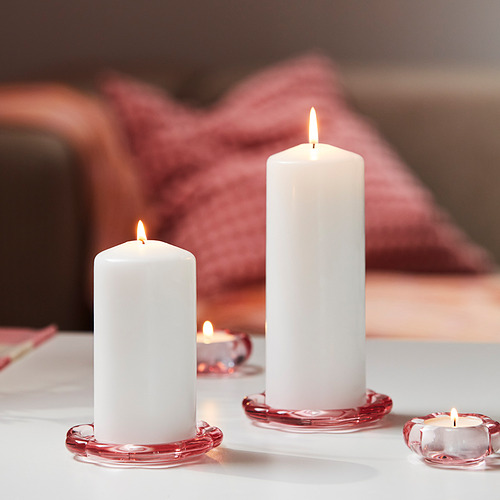 Tres velas de pilar encendidas sobre soportes de vidrio rojo.
