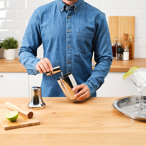 El hombre sirve de una coctelera. Sobre mesa de madera con limas, vasos y herramientas de madera.