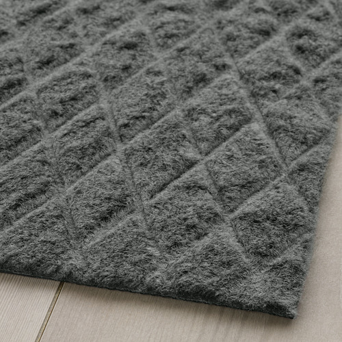 Felpudo gris texturizado con estampado de rombos sobre suelo de madera.