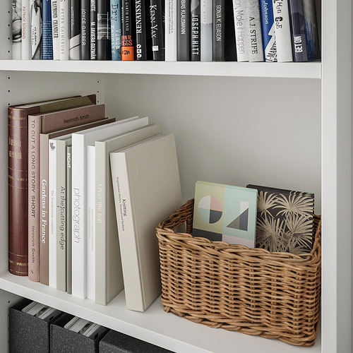Estantería blanca con cesta tejida que contiene libros de colores, libros apilados y libros de lomo negro debajo.