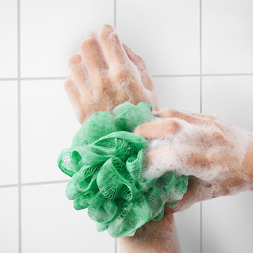 A mano usando puff corporal de malla verde con jabón, exfoliando la piel, creando espuma.