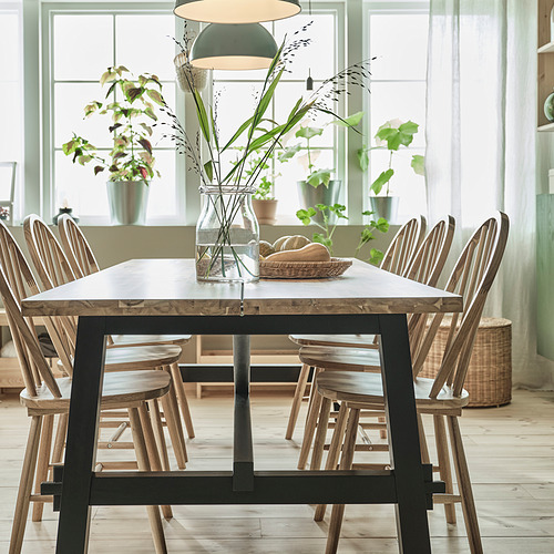 Mesa de comedor SKOGSTA, marrón oscuro, madera y metal, rectangular, con sillas, centro de mesa, plantas, ventana grande.